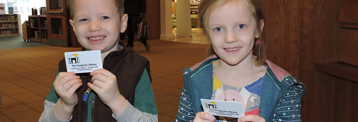 Two young children holding up their library cards and smiling